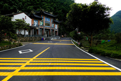 乡村道路建设整洁有序，黑色平整的沥青路面，划有行人斑马线和黄色的减速带，乡村环境治理大大提升乡村生活