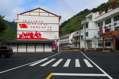 乡村道路建设整洁有序，黑色平整的沥青路面，划有行人斑马线和黄色的减速带，乡村环境治理大大提升乡村生活