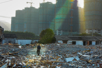 图八：拍摄于2021年月2月4日，一位正在拆除后的废墟地上走过，隔避就是正在建设的高楼的小区。